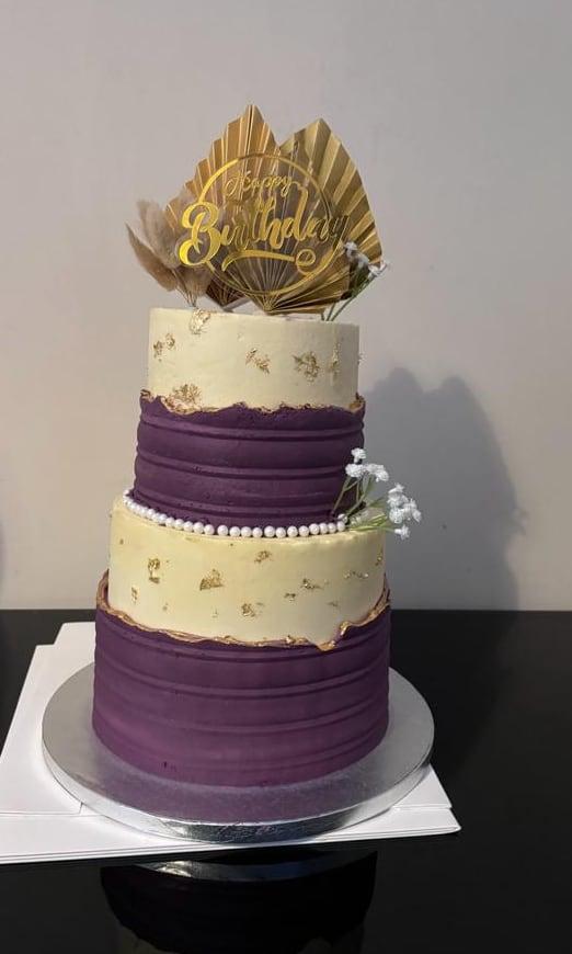 A three-tier purple and ivory cake with gold leaf and piped pearl detail