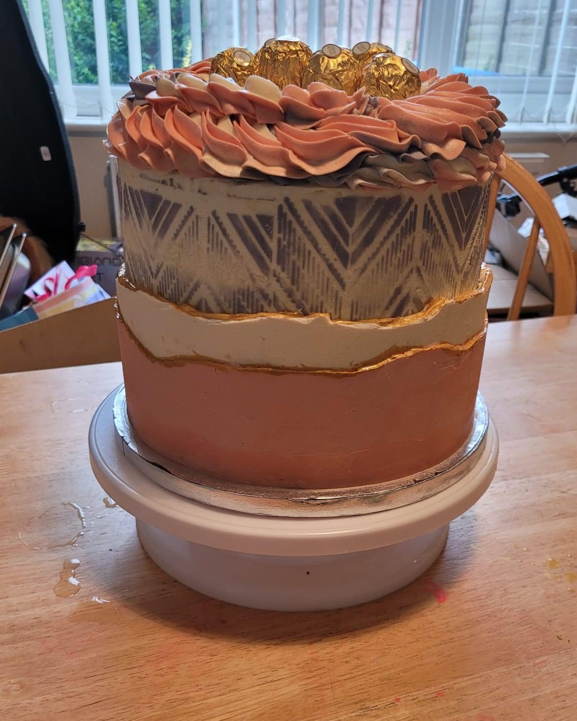 A copper and ivory cake with a stencilled chevron band, gold leaf edge and piped rosettes