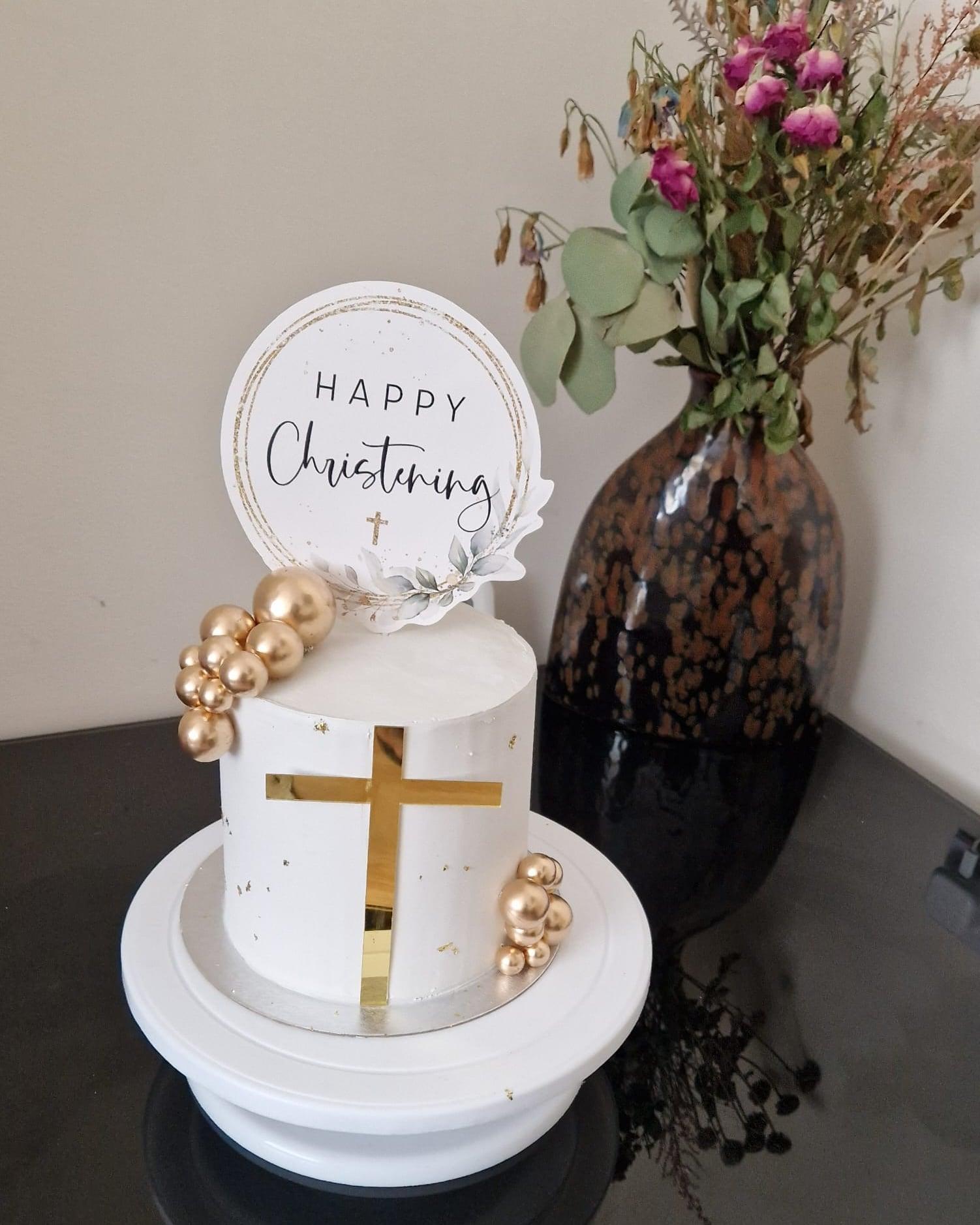 A white christening cake finished with a gold cross and gilded spheres
