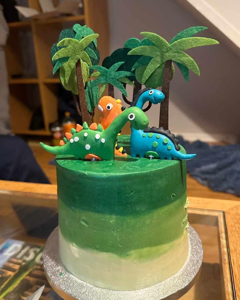 A green ombre cake topped with hand-modelled dinosaurs and sugar palm trees