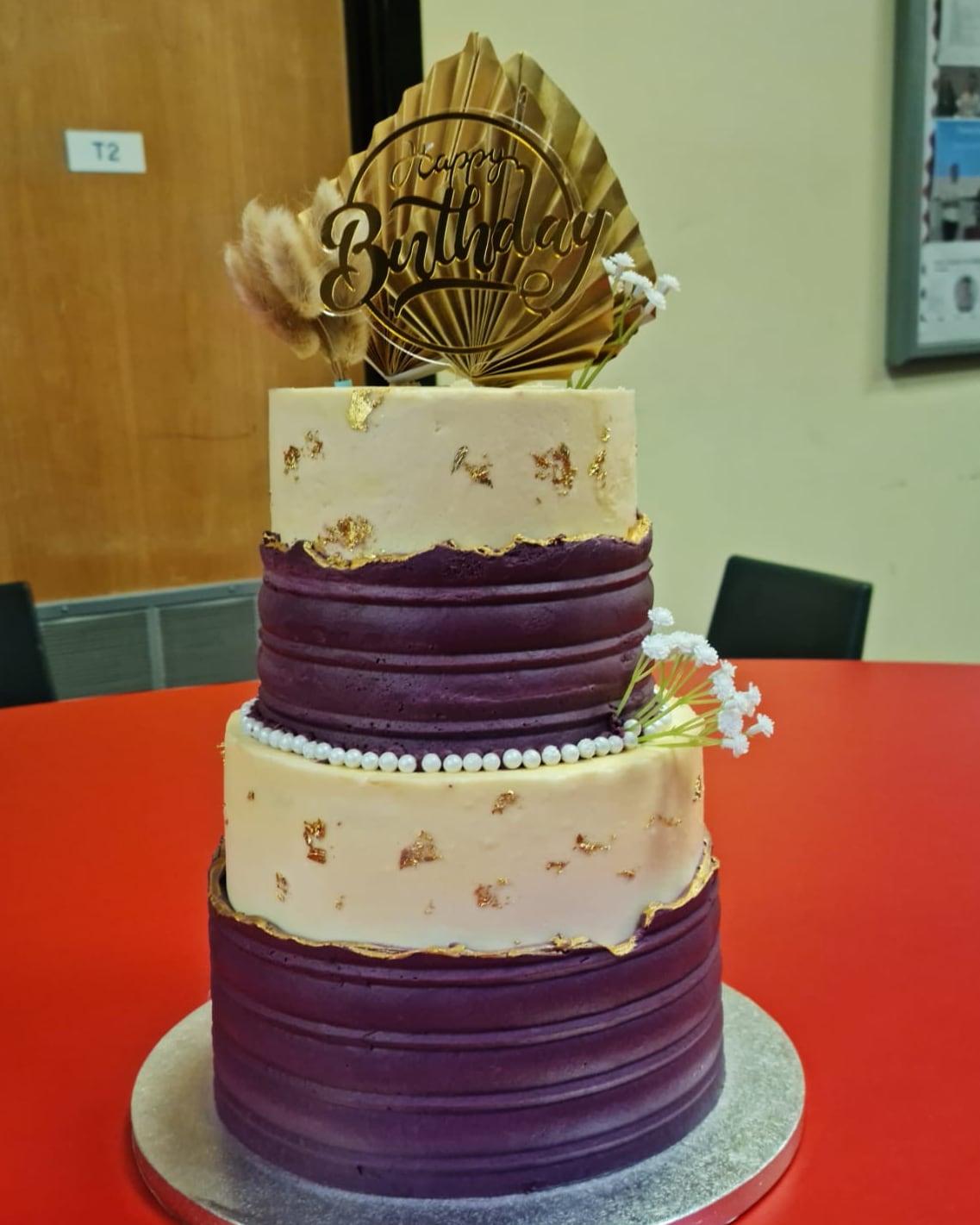 A three-tier plum and ivory celebration cake finished with gold leaf and piped pearls