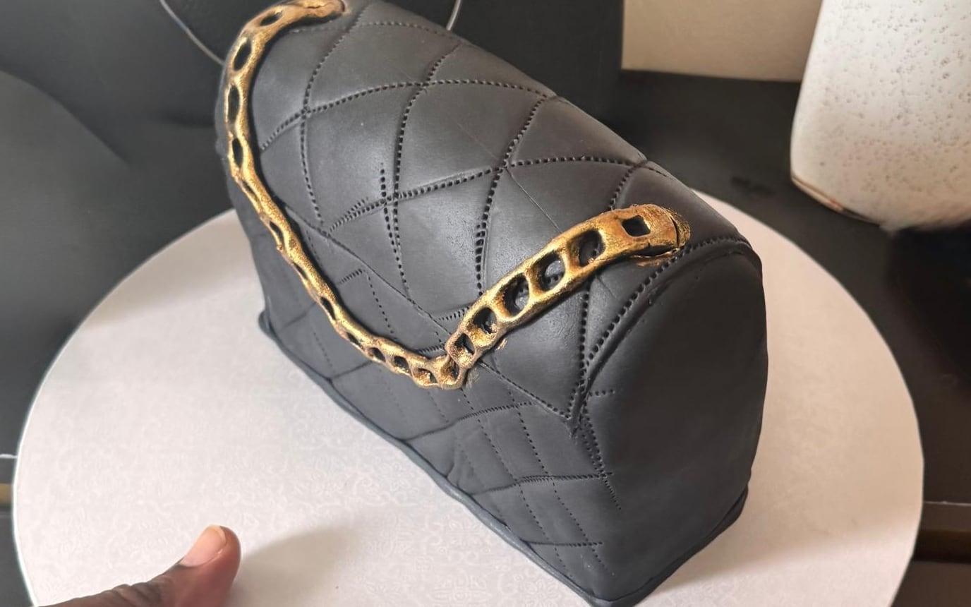 A hand-sculpted quilted handbag cake with a gold chain strap, seen from three quarters