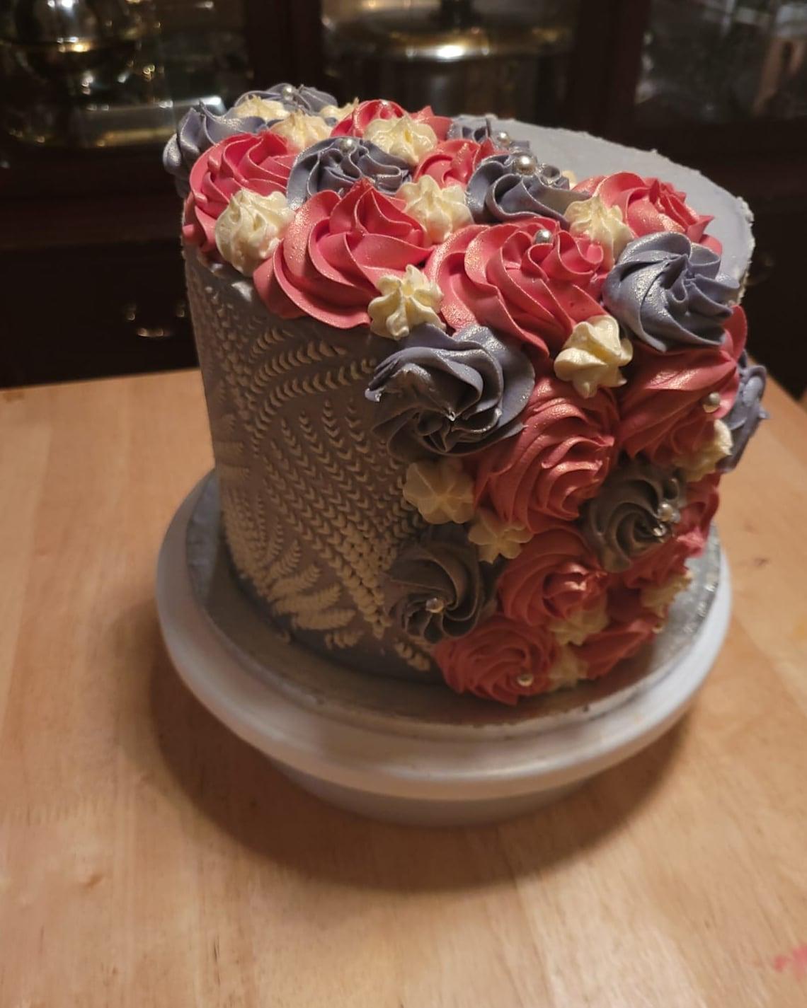 A copper cake with lace-textured piping and a spill of rose and slate buttercream swirls