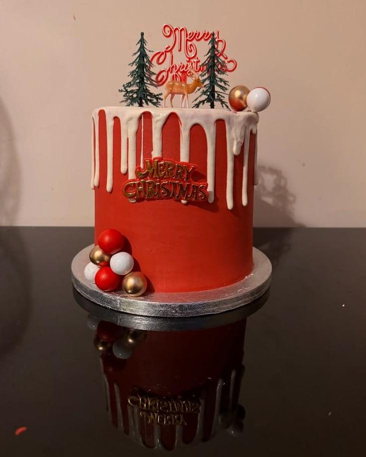A ruby red Christmas cake with an ivory drip, baubles and a winter topper