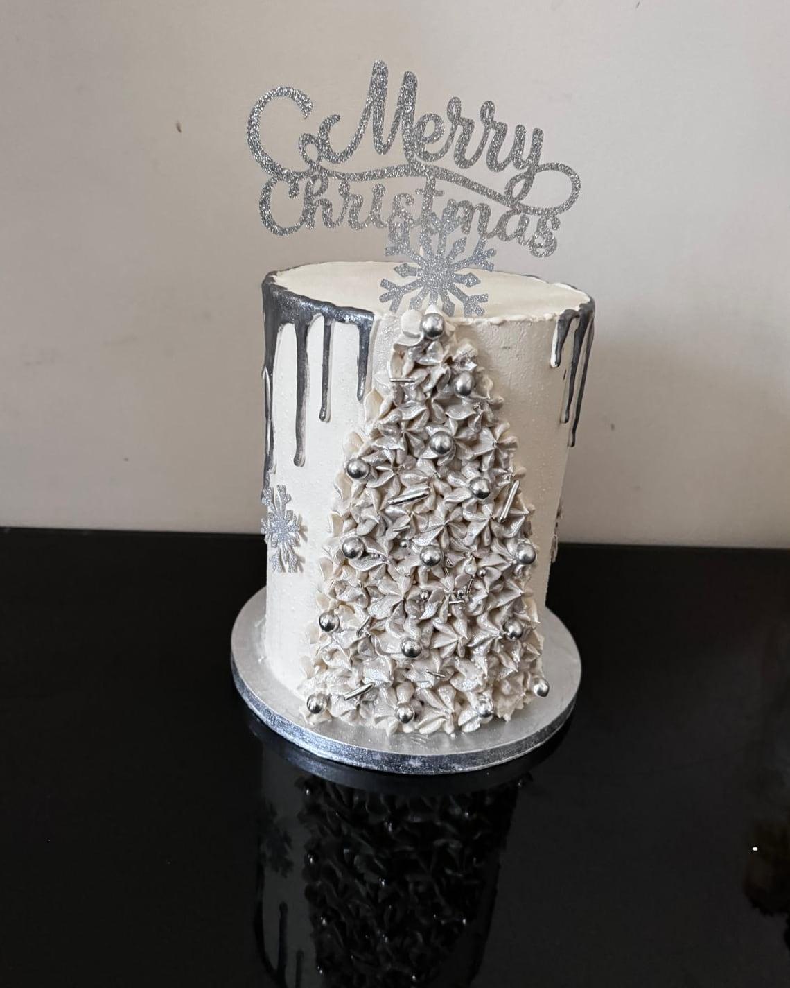 An ivory Christmas cake with a poured silver drip and a hand-piped tree