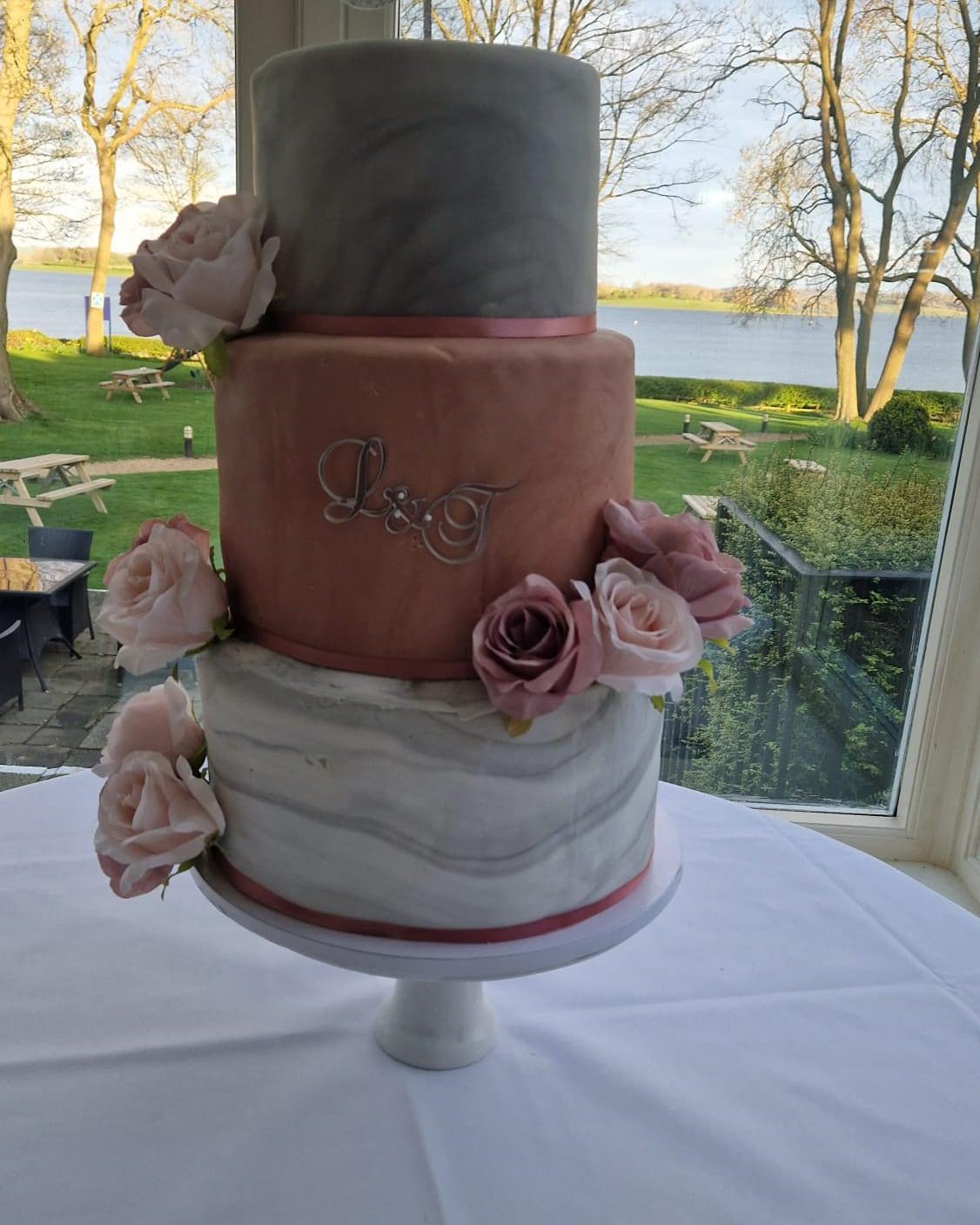 A three-tier marble wedding cake with a monogrammed terracotta tier and dusty sugar roses