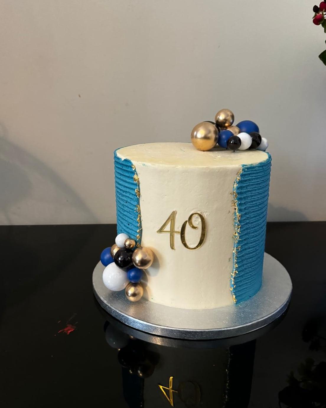 An ivory fortieth birthday cake with ribbed teal panels and navy and gold spheres