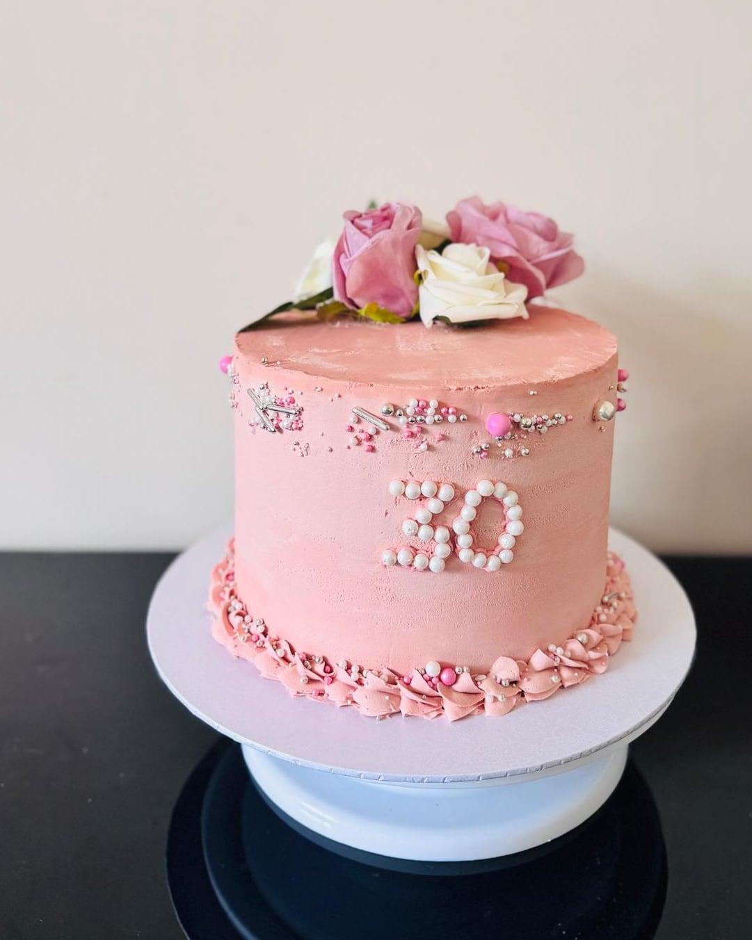 A blush thirtieth birthday cake with a piped pearl number and sugar roses